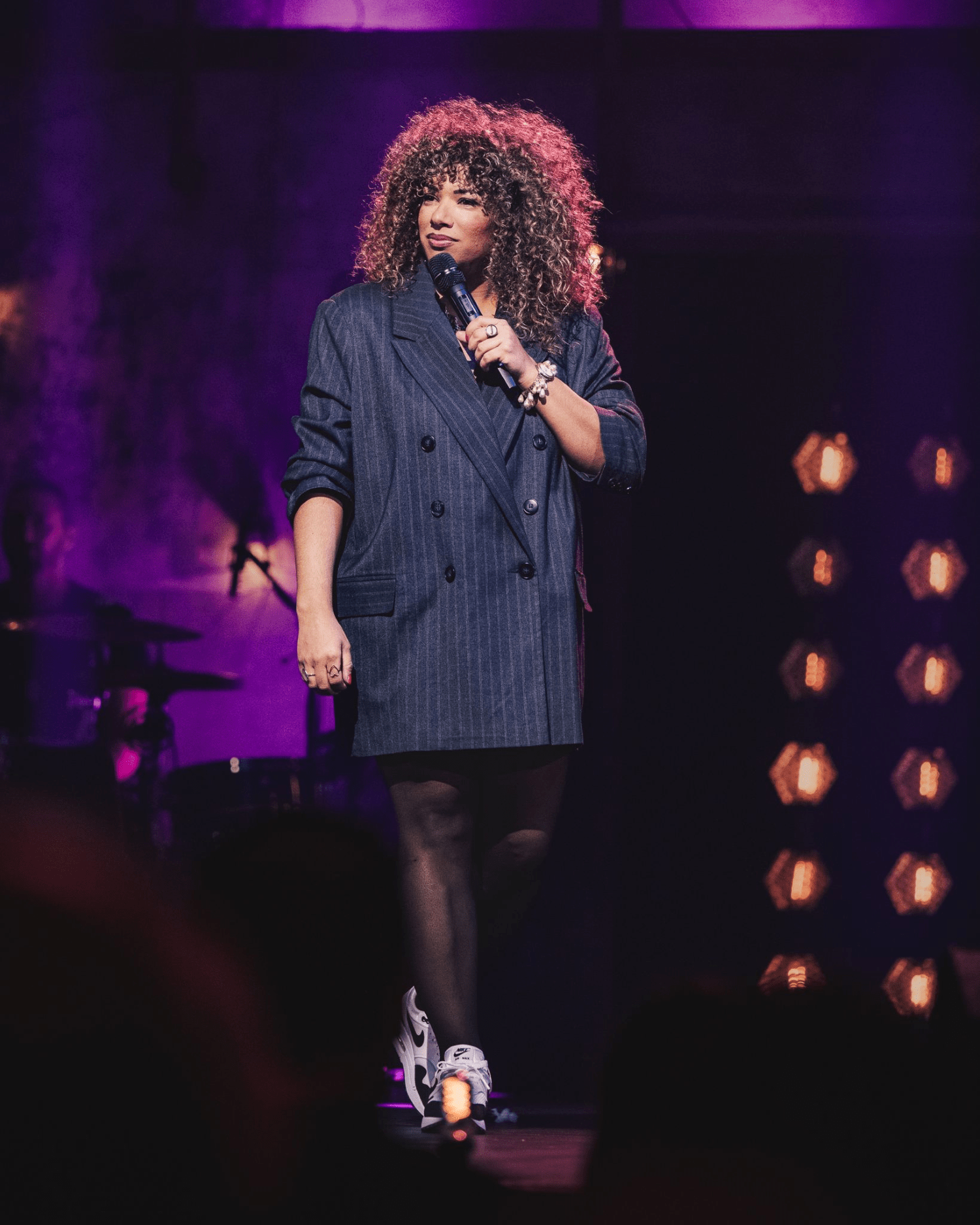 Emy on stage with microphone against a dark background with stage lights